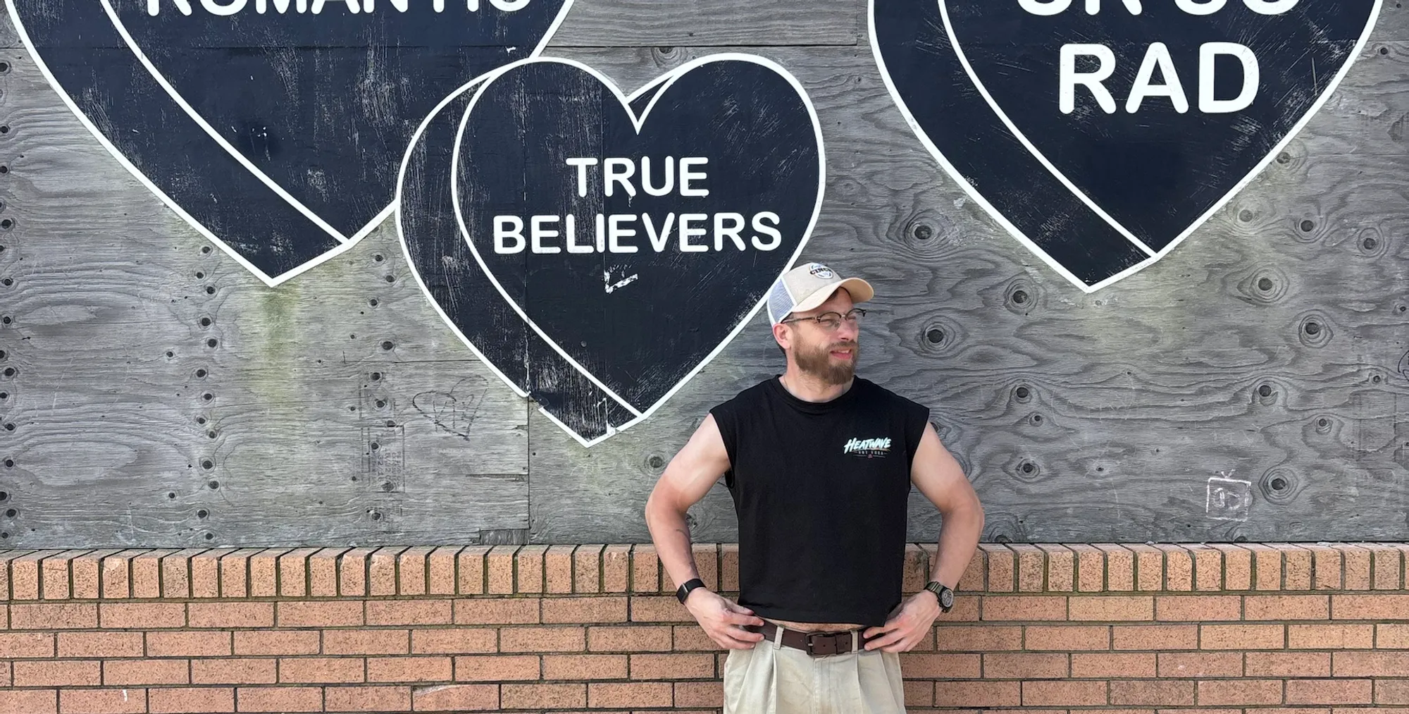 Joshua Herrington against a mural of conversation hearts reading Hopeless Romantic, True Believers, Ur So Rad