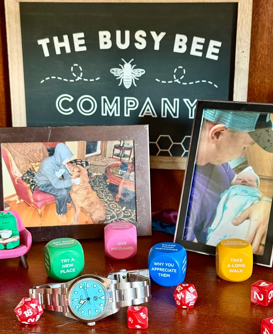 A shelf holding framed photos, conversation dice, polyhedral dice and a watch