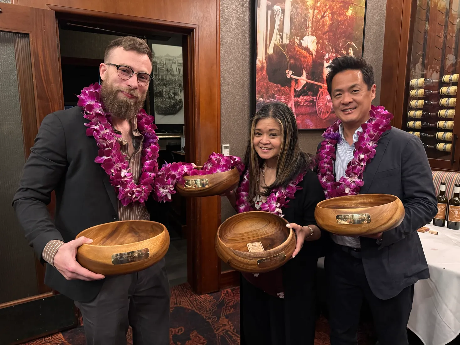 Joshua Herrington and two colleagues wearing orchid leis and holding engraved koa bowls